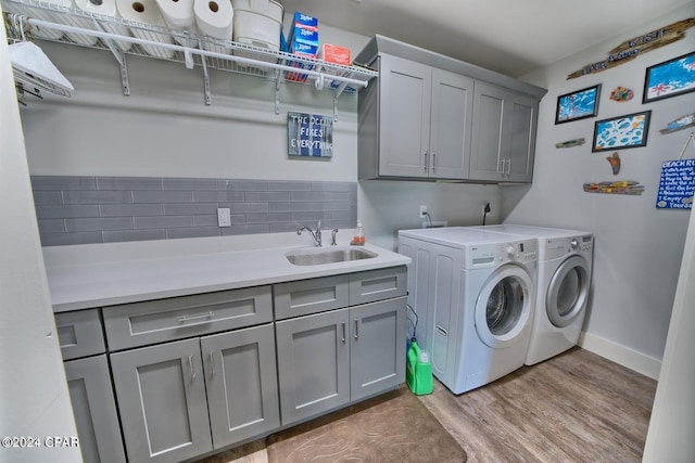 laundry room with cabinet space, light wood-style flooring, a sink, washer and dryer, and baseboards