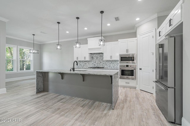 kitchen with appliances with stainless steel finishes, backsplash, light stone counters, an island with sink, and white cabinets