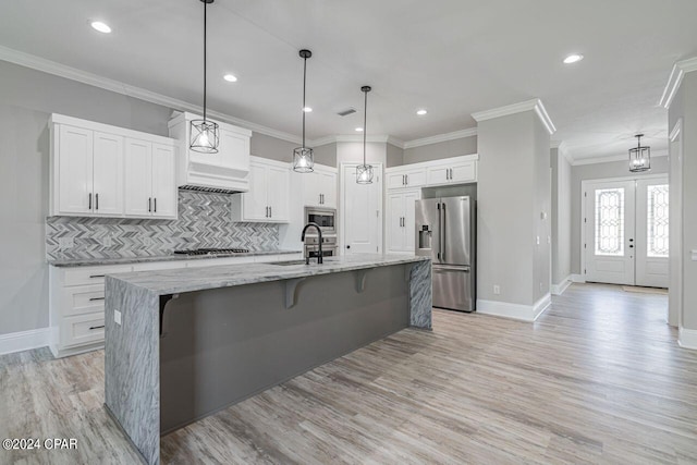 kitchen with stainless steel appliances, light stone countertops, an island with sink, white cabinets, and decorative backsplash