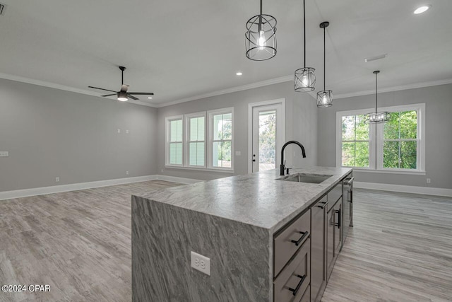 kitchen with pendant lighting, sink, ornamental molding, a kitchen island with sink, and light stone countertops