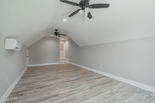 bonus room with a wall mounted air conditioner, a textured ceiling, and light wood-type flooring