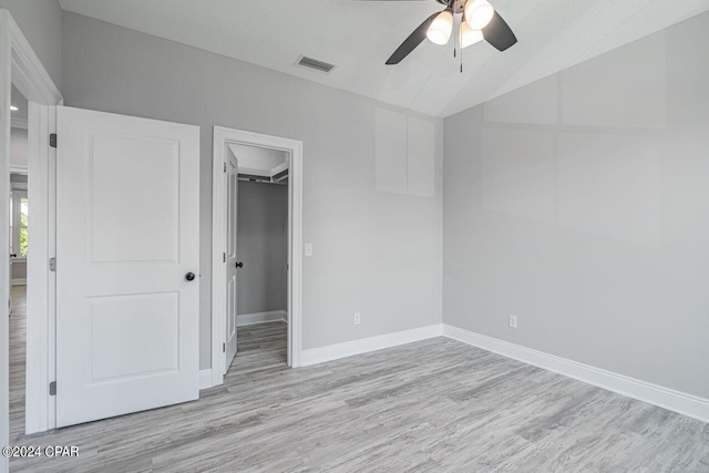 unfurnished bedroom with ceiling fan, a spacious closet, light hardwood / wood-style floors, and a closet