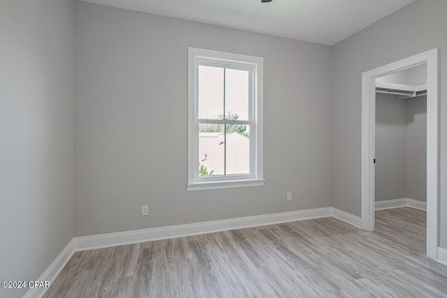 unfurnished bedroom featuring multiple windows, a spacious closet, light wood-type flooring, and a closet