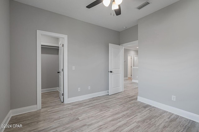 unfurnished bedroom featuring a closet, a walk in closet, ceiling fan, and light hardwood / wood-style floors