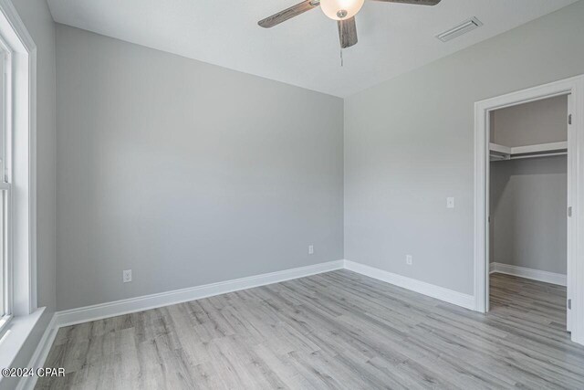 unfurnished bedroom with light hardwood / wood-style floors, a spacious closet, ceiling fan, and a closet