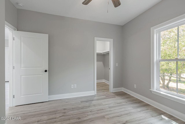 unfurnished bedroom with a closet, a spacious closet, ceiling fan, and light wood-type flooring