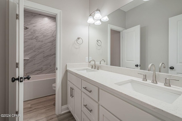 full bathroom featuring tiled shower / bath combo, toilet, hardwood / wood-style floors, and dual bowl vanity