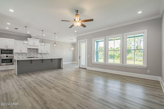 kitchen with a breakfast bar area, appliances with stainless steel finishes, backsplash, a kitchen island with sink, and light wood-type flooring