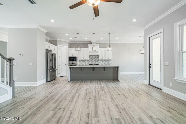 kitchen featuring appliances with stainless steel finishes, light hardwood / wood-style flooring, tasteful backsplash, white cabinetry, and a spacious island