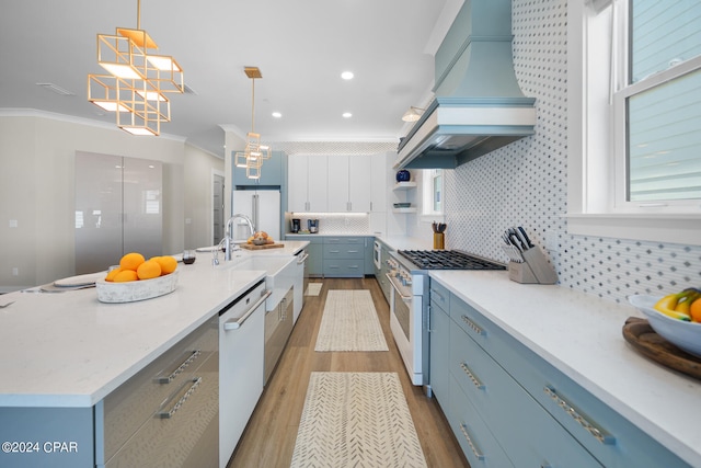 kitchen with decorative light fixtures, decorative backsplash, an island with sink, white appliances, and custom range hood