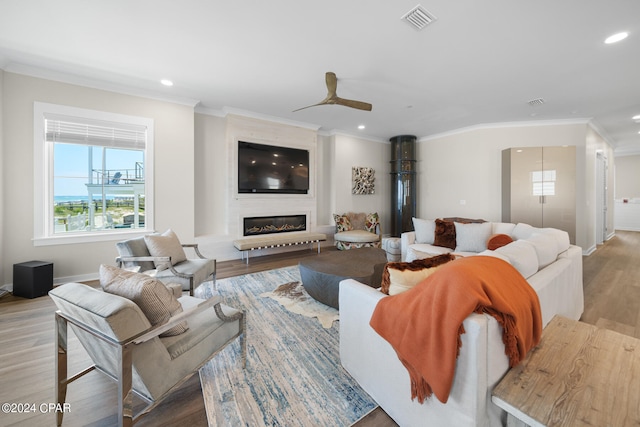 living room featuring ceiling fan, light hardwood / wood-style flooring, a large fireplace, and ornamental molding