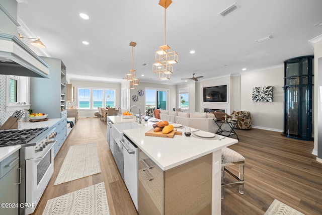 kitchen with hardwood / wood-style flooring, custom range hood, a center island with sink, and a kitchen bar