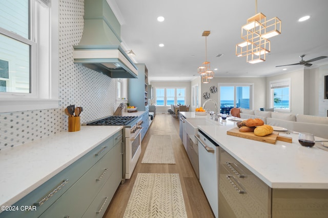 kitchen with light hardwood / wood-style flooring, backsplash, custom exhaust hood, gas range, and a center island with sink