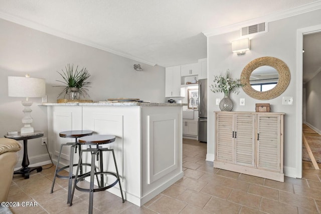 kitchen featuring crown molding, kitchen peninsula, a kitchen bar, and white cabinets