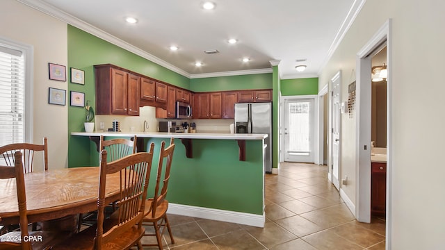 kitchen with a kitchen breakfast bar, appliances with stainless steel finishes, kitchen peninsula, ornamental molding, and tile patterned floors