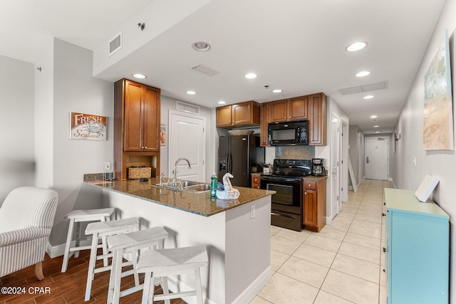 kitchen with visible vents, a peninsula, a sink, black appliances, and brown cabinets