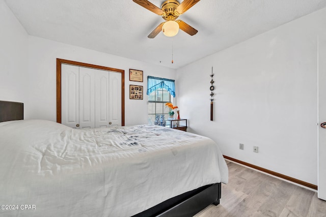 bedroom with light wood-type flooring, a textured ceiling, ceiling fan, and a closet