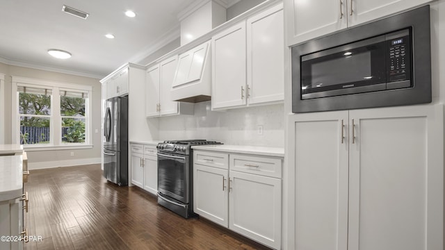 kitchen with custom range hood, appliances with stainless steel finishes, dark wood-type flooring, crown molding, and white cabinets