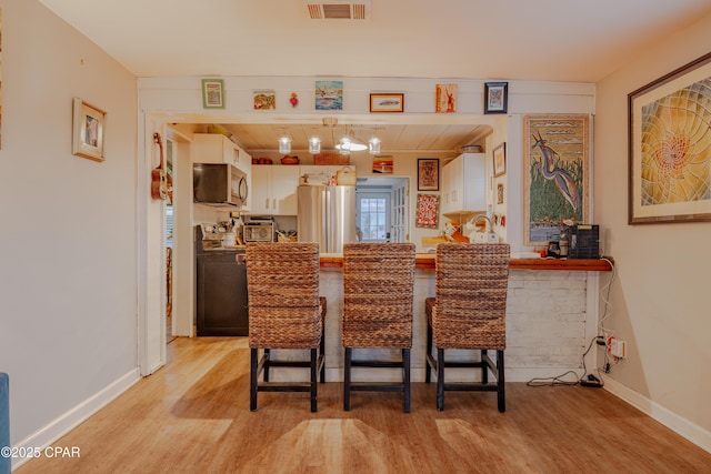 bar with light wood-type flooring, stainless steel appliances, and white cabinetry