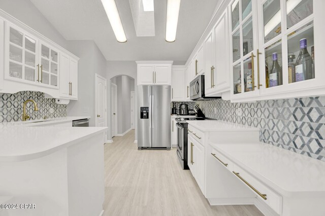 kitchen featuring a skylight, white cabinetry, sink, stainless steel appliances, and light hardwood / wood-style floors