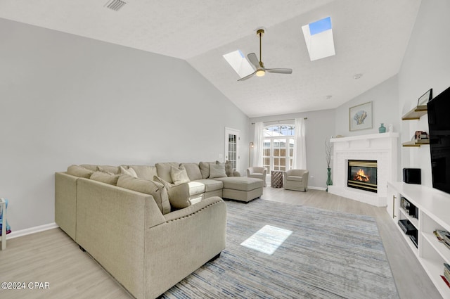 living room featuring a fireplace, light wood-type flooring, vaulted ceiling, and ceiling fan