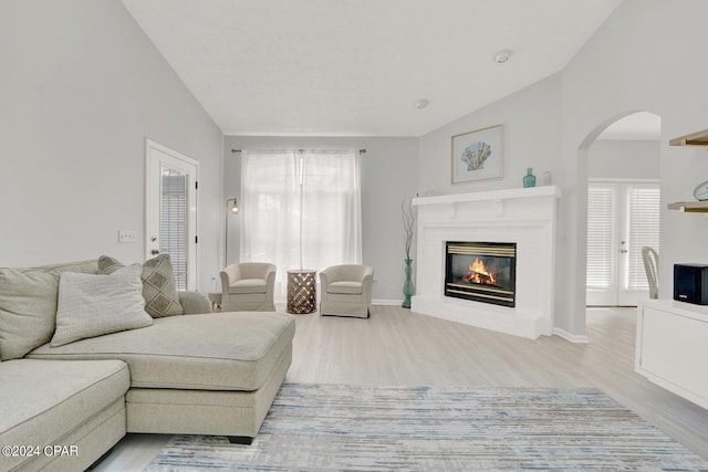 living room featuring plenty of natural light, vaulted ceiling, wood-type flooring, and a brick fireplace