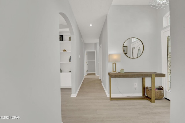 corridor featuring built in shelves, light hardwood / wood-style floors, and an inviting chandelier