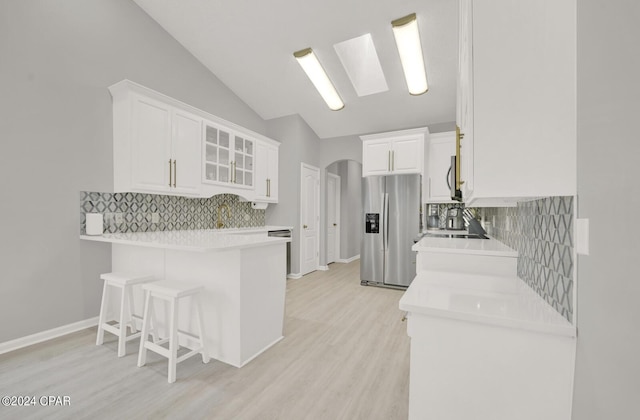 kitchen featuring a breakfast bar, white cabinets, stainless steel refrigerator with ice dispenser, vaulted ceiling with skylight, and kitchen peninsula