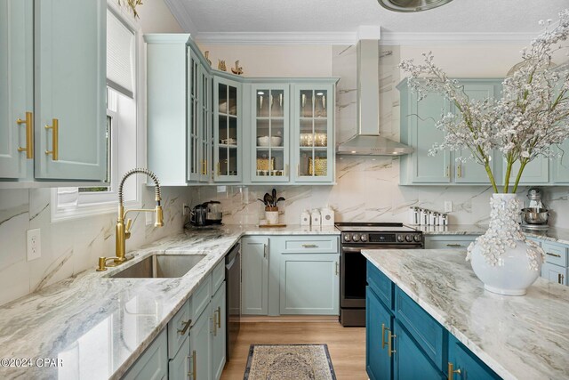 kitchen with stainless steel appliances, light stone counters, wall chimney exhaust hood, and light hardwood / wood-style flooring