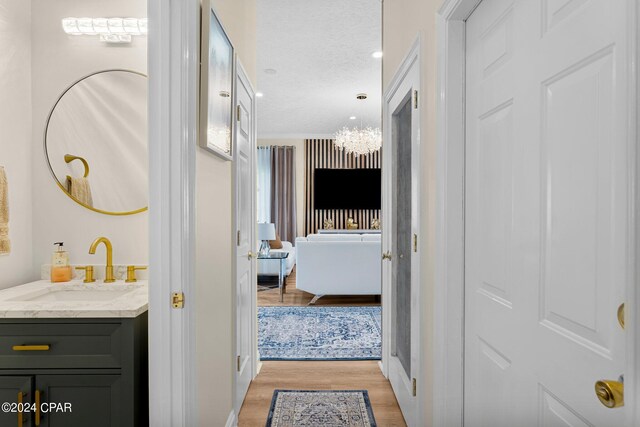 hallway with a chandelier, light hardwood / wood-style floors, sink, and a textured ceiling