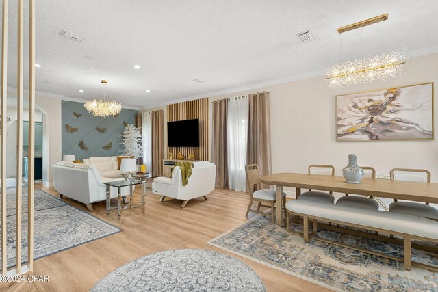 dining area with an inviting chandelier, crown molding, a textured ceiling, and light hardwood / wood-style floors