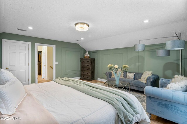 bedroom with vaulted ceiling, a textured ceiling, and light wood-type flooring