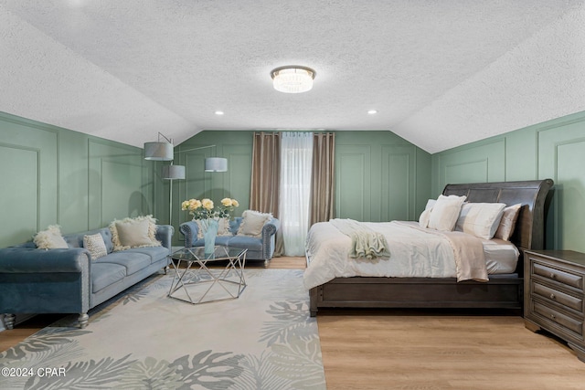 bedroom with vaulted ceiling, light wood-type flooring, and a textured ceiling