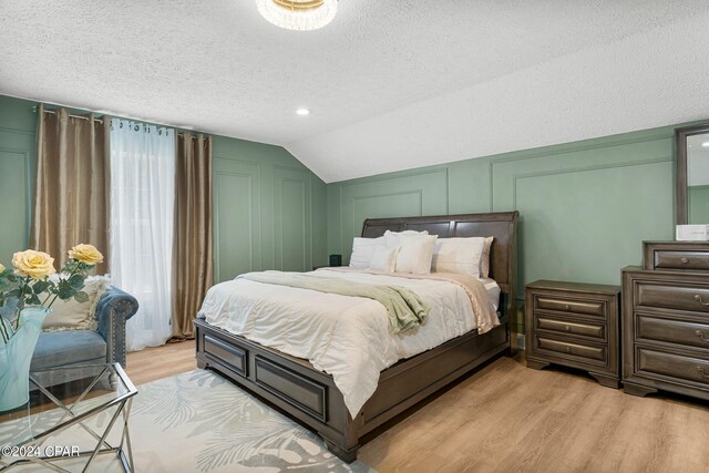 bedroom with light wood-type flooring, lofted ceiling, and a textured ceiling