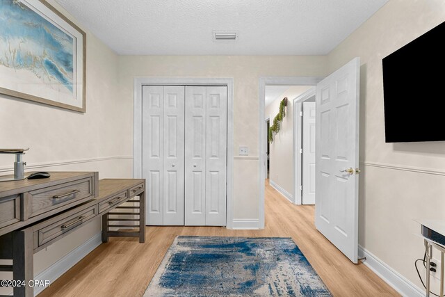 interior space with a textured ceiling, light hardwood / wood-style flooring, and a closet