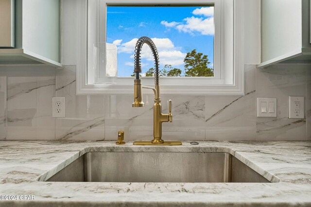 interior details featuring white cabinets, backsplash, and light stone countertops