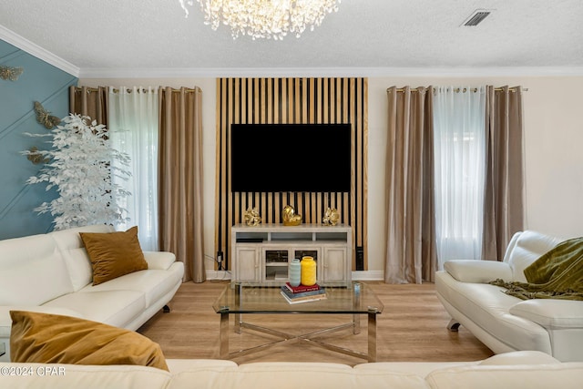 living room with an inviting chandelier, a textured ceiling, crown molding, and light wood-type flooring