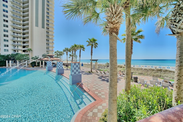 view of swimming pool with a patio, a water view, and a view of the beach