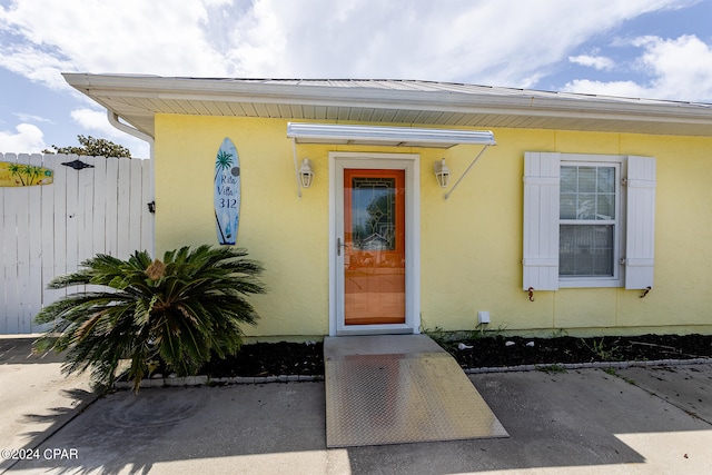 entrance to property featuring fence and stucco siding