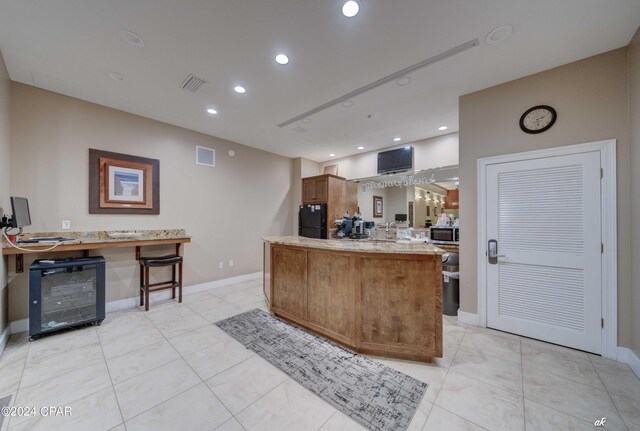 kitchen featuring black refrigerator, light tile patterned floors, a breakfast bar, and kitchen peninsula