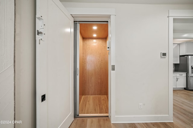 hallway with elevator and light hardwood / wood-style flooring