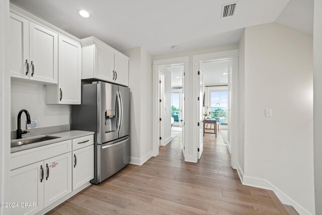 kitchen featuring sink, white cabinets, stainless steel fridge, light wood-type flooring, and vaulted ceiling