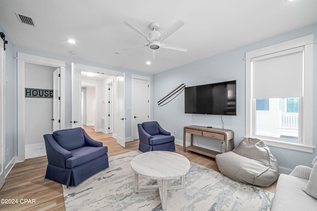 living room with a barn door, wood-type flooring, and ceiling fan