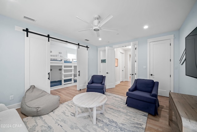 living room featuring wood-type flooring, a barn door, and ceiling fan