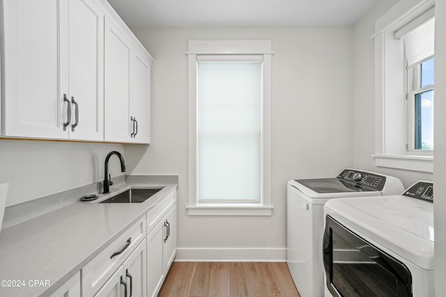 clothes washing area with cabinets, sink, light wood-type flooring, and washer and clothes dryer