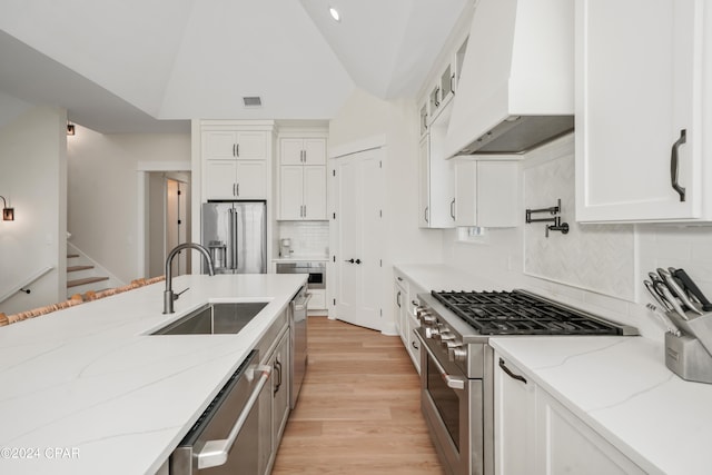 kitchen with vaulted ceiling, white cabinets, sink, custom range hood, and high quality appliances