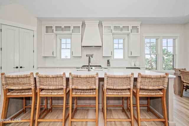 kitchen with white cabinetry, light wood-type flooring, custom exhaust hood, and a breakfast bar