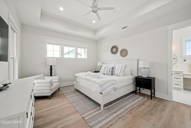 bedroom featuring light hardwood / wood-style flooring, multiple windows, ceiling fan, and a tray ceiling