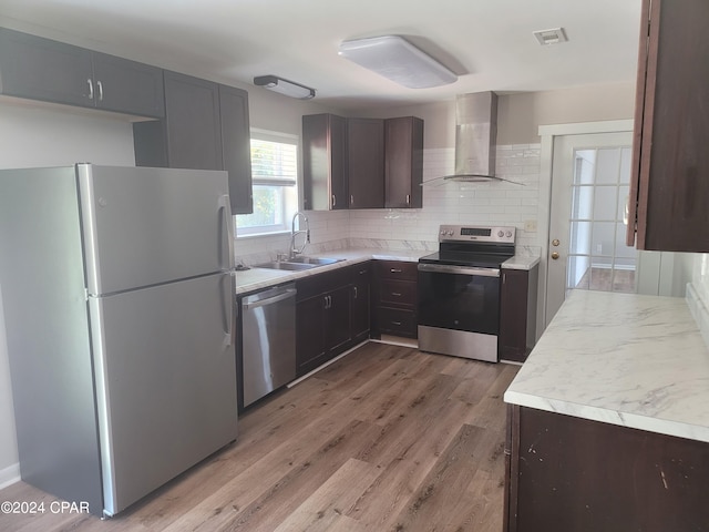 kitchen with wall chimney range hood, decorative backsplash, light hardwood / wood-style flooring, sink, and stainless steel appliances