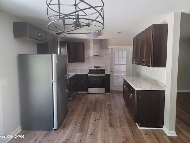 kitchen with appliances with stainless steel finishes, wall chimney exhaust hood, decorative backsplash, light hardwood / wood-style flooring, and an inviting chandelier